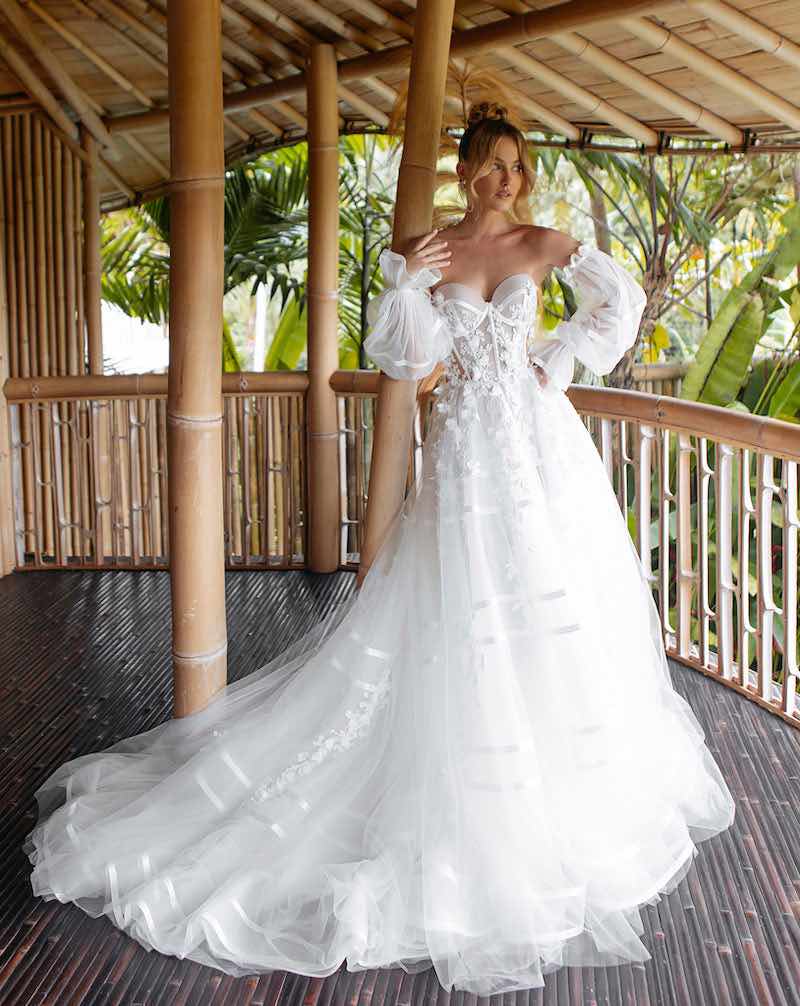 In questa foto una modella indossa un abito da sposa ad A Agnieszka Swiatly 2024 in tulle a righe con maniche a sbuffo staccabili e ramage di foglie che scendono dal busto