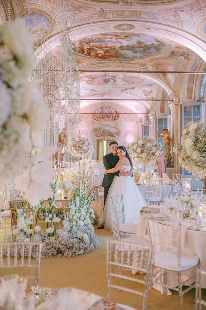 In questa foto gli sposi Carlotta e Federico si abbracciano nella Galleria delle Stagioni a Villa Faraggiana allestita per il loro matrimonio da Giovanna Damonte con fiori total white, elementi riflettenti e di colore rosa