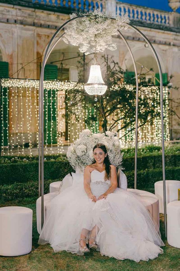 In questa foto la sposa Carlotta seduta su uno dei divanetti in velluto di colore rosa sormontati da un lampadario chandelier che componevano i salottini realizzati da Giovanna Damonte