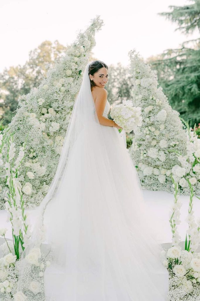 In questa foto la sposa Carlotta posa davanti all'altare composto da due ali di fiori di colore bianco realizzato dalla Wedding Planner Giovanna Damonte 