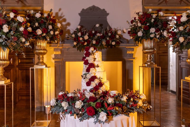 In questa foto una torta nuziale a piani decorata con crema al burro di colore bianco e fiori freschi di colore rosso e bianco