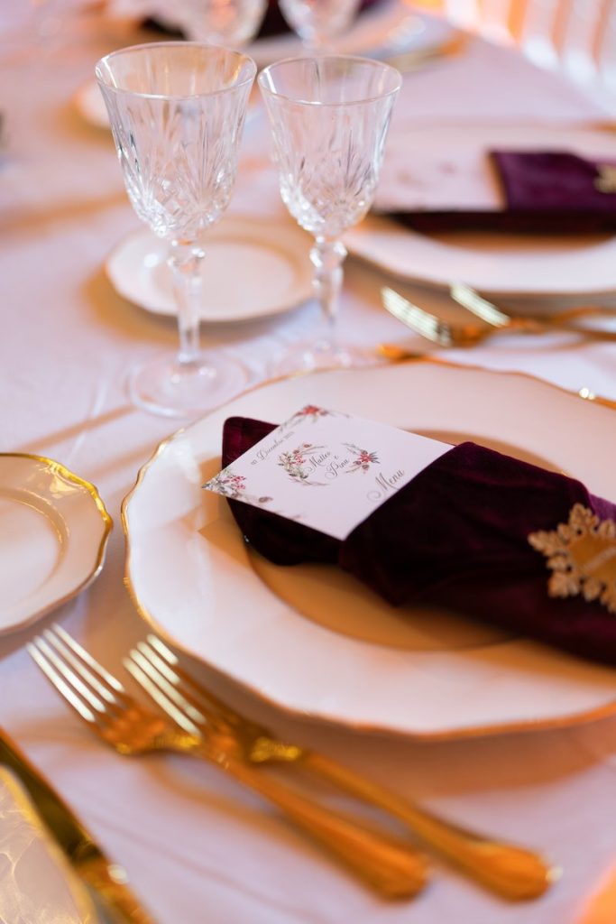 In questa foto il dettaglio della mise en place di un matrimonio a tema Natale realizzata da Stefano Miranda con posate di colore oro, piatti di ceramica, bicchieri di cristallo e tovagliolo di colore bordeaux