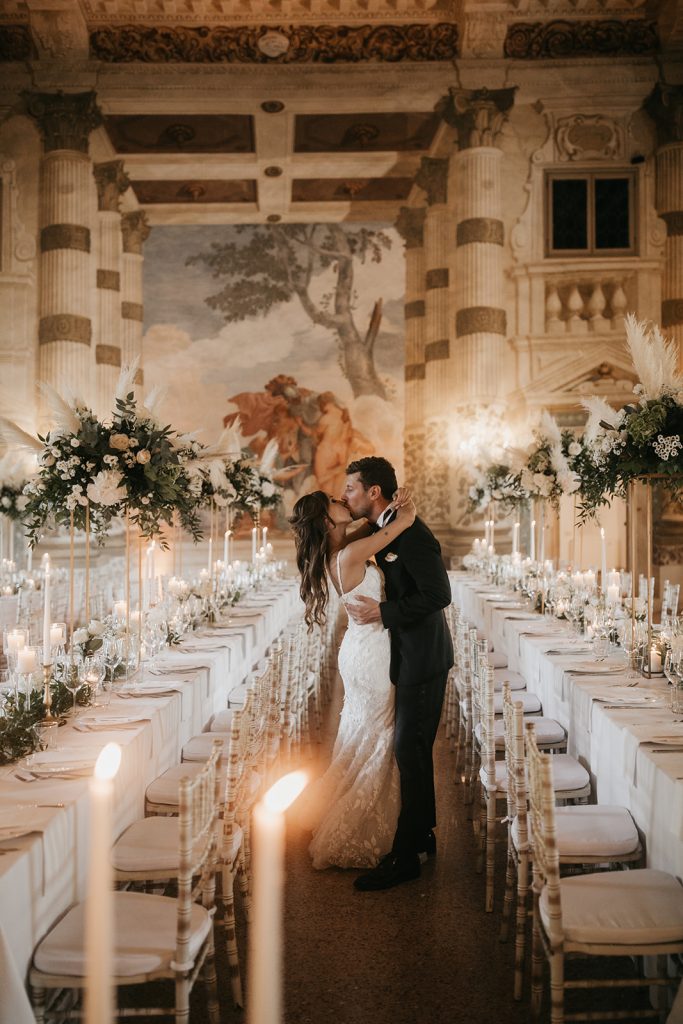 Due sposi si baciano tra i tavoli della location scelta per la loro festa in uno scatto realizzato da Matteo Rossi Fotografia