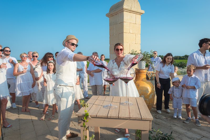 In questa foto due sposi circondati dai loro invitati eseguono il Rito di Dioniso durante il loro Wine Wedding  a Masseria Cuturi 