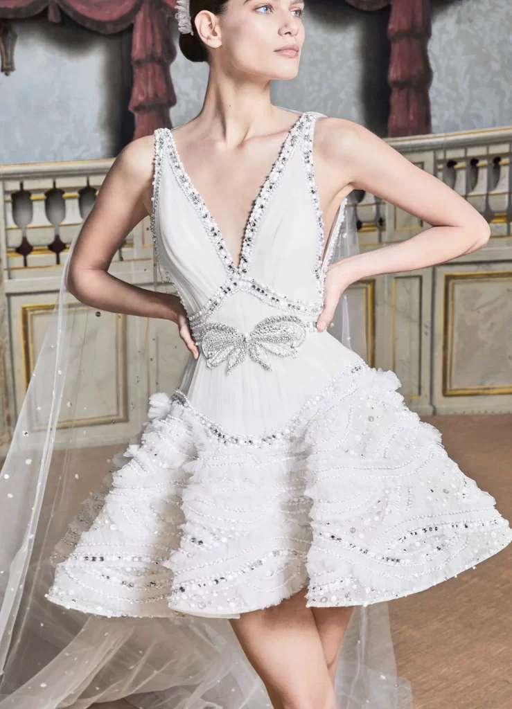 In questa foto la modella indossa un abito da sposa Elie Saab 2024 corto con fiocco e scollo a V.