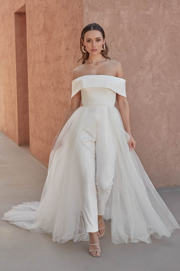 In questa immagine una jumpsuit da sposa con sovragonna della collezione Adore by Justin Alexander 2024.