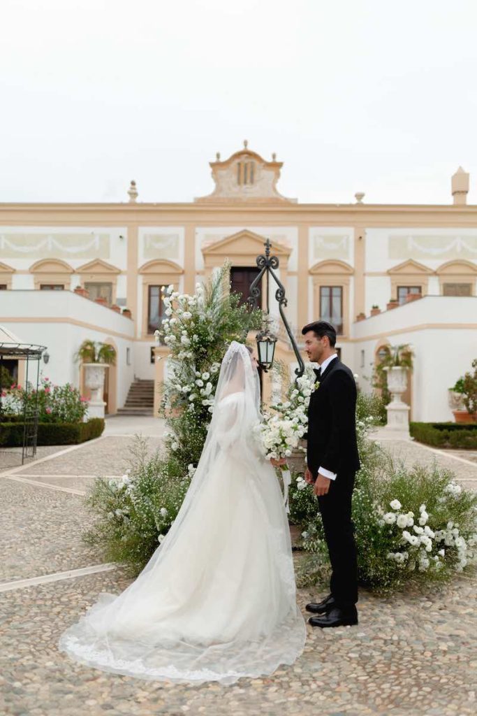 In questa foto due sposi durante uno dei matrimoni simbolici a Villa del Gattopardo, allestito davanti all'antico pozzo davanti alla facciata principale della Villa e decorato con fiori bianchi
