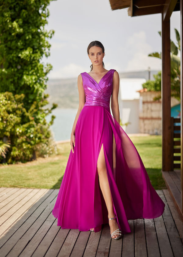 In questa foto una modella indossa un vestito per le invitate al matrimonio più giovani fucsia, con spacco. L'abito è di Musani per il 2024