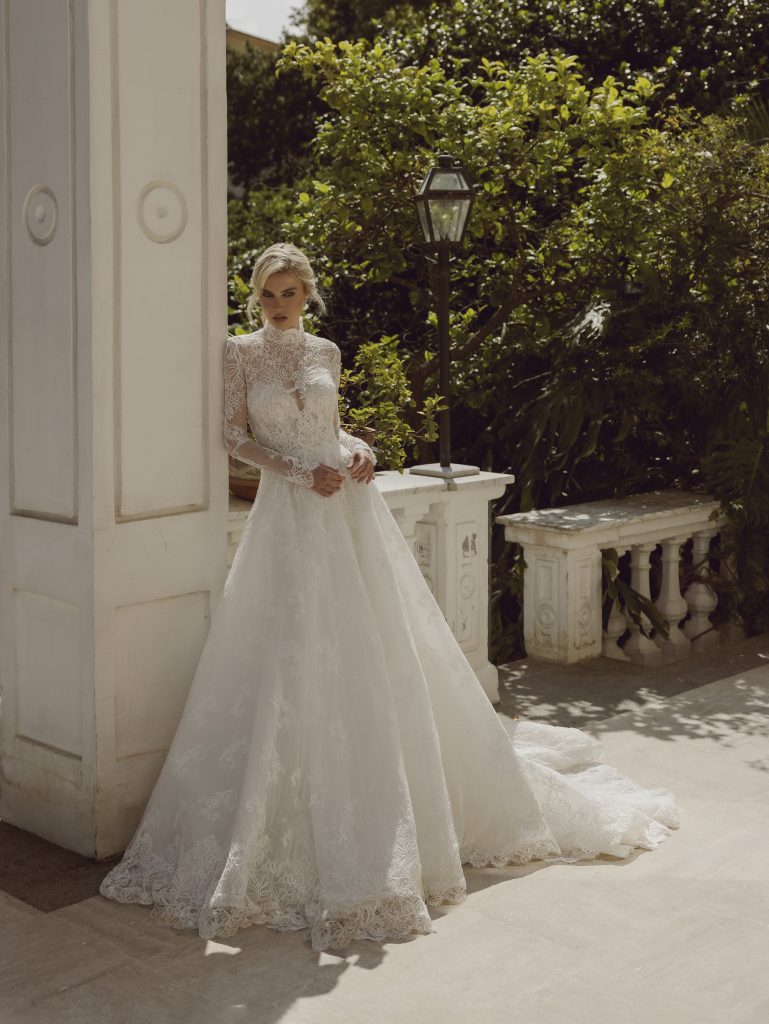 In questa foto la modella indossa un abito Ricca sposa 2024 di pizzo a maniche lunghe.