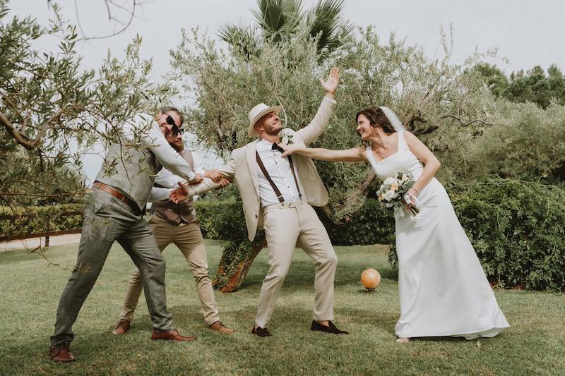 In questa foto una sposa scherza con lo sposo e i testimoni in un giardino di ulivi