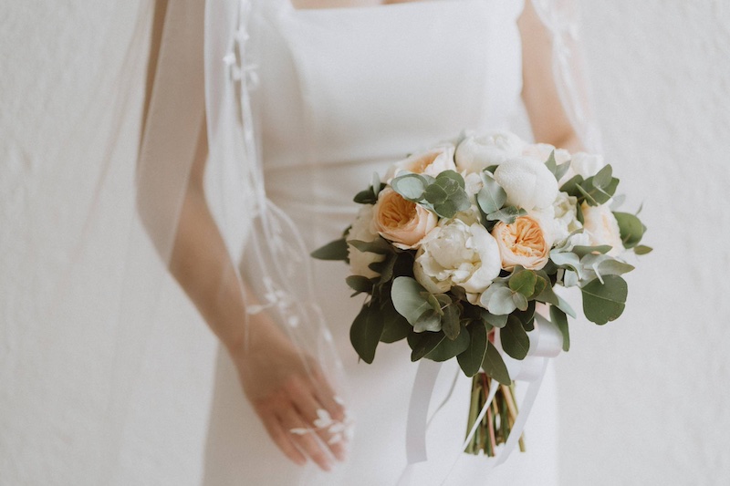 In questa foto il dettaglio di una sposa con in mano un bouquet di peonie di colore bianco e rose inglesi di colore rosa cipria