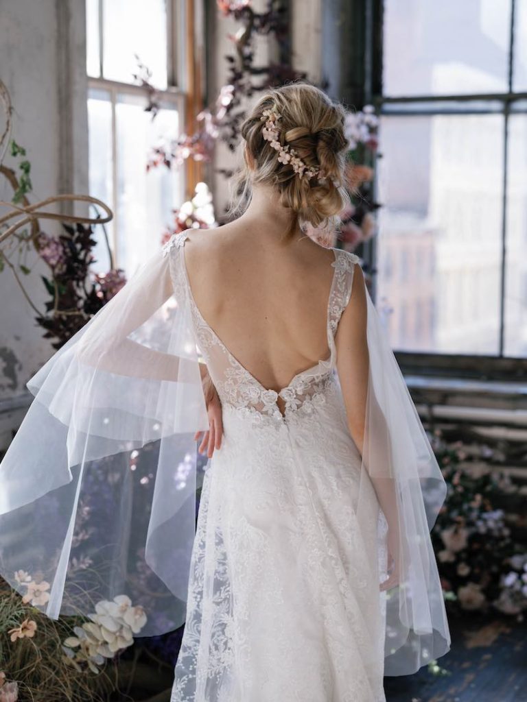 In questa foto una modella di spalle mostra un'acconciatura da sposa con treccia posteriore obliqua e un fermaglio con fiori di colore pastello