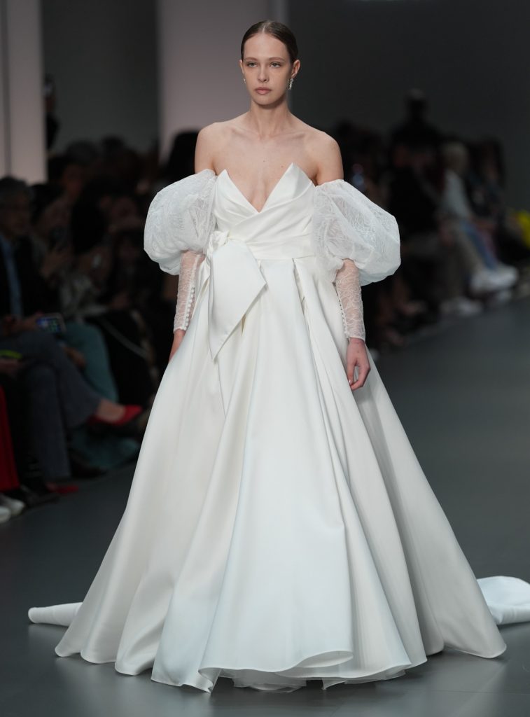 In questa immagine un abito da sposa Helena 2025 ampio, con maniche in pizzo.