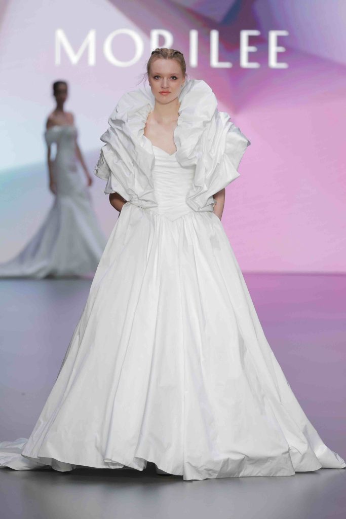 In questa immagine un abito da sposa Morilee 2025 con maxi coprispalle. 