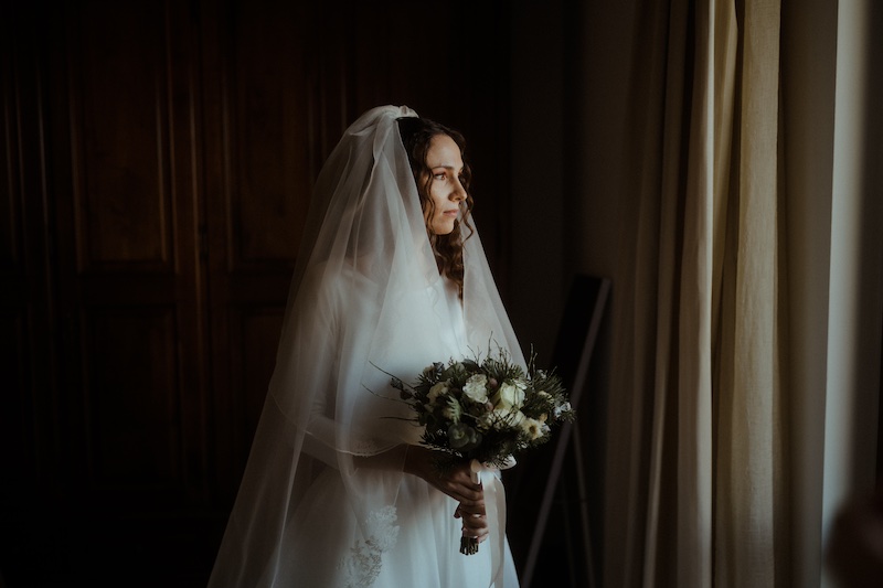 In questa foto di Alessio Bazzichi una sposa posa con il suo bouquet davanti ad una finestra