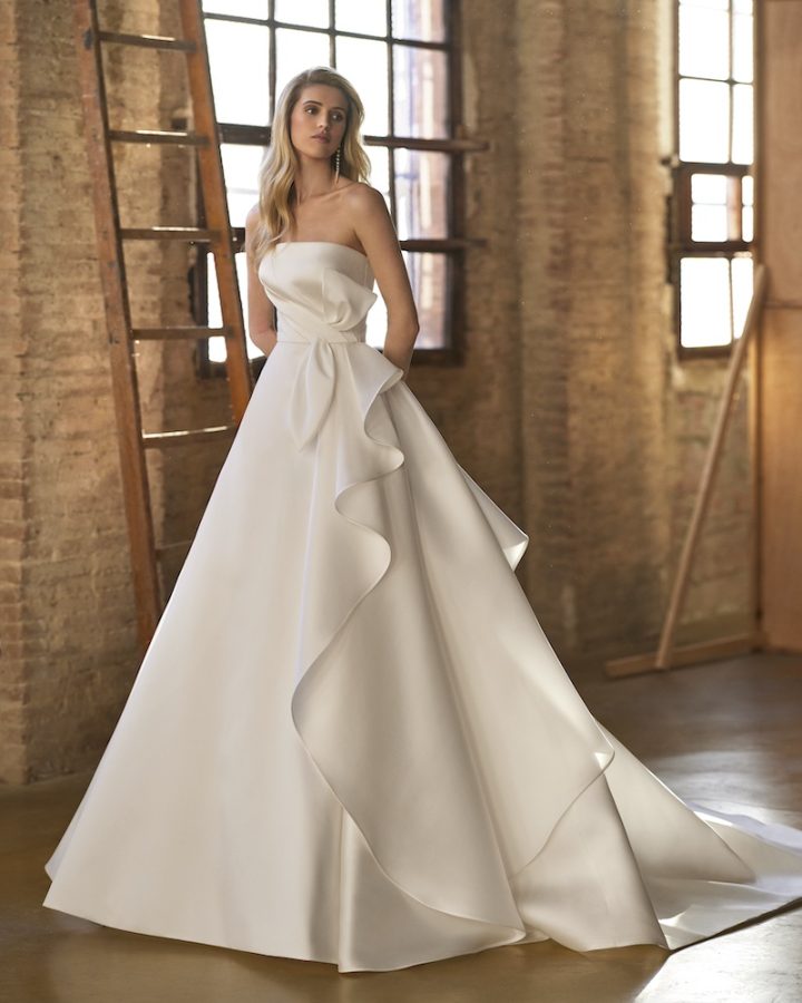 In questa foto una modella posa indossando un abito da sposa Aire Atelier 2025 ad A in mikado con strati sovrapposti