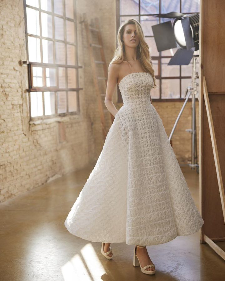 In questa foto una modella posa indossando un abito da sposa Aire Atelier 2025 midi in tulle intrecciato effetto 3D