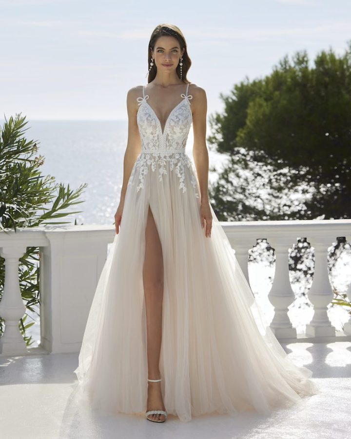 In questa foto una modella posa indossando un abito da sposa Aire Chic 2025 con gonna ad A in tulle e spacco e corpetto con scollatura a V