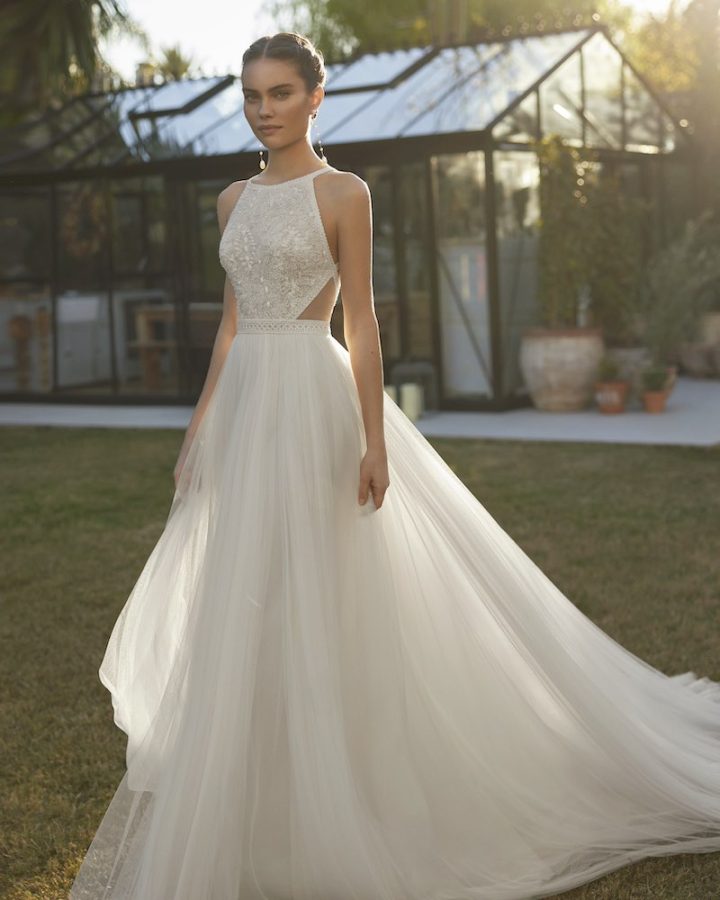 In questa foto una modella posa  indossando un abito da sposa Aire Boho 2025 con tagli cut out laterali e gonna in tulle