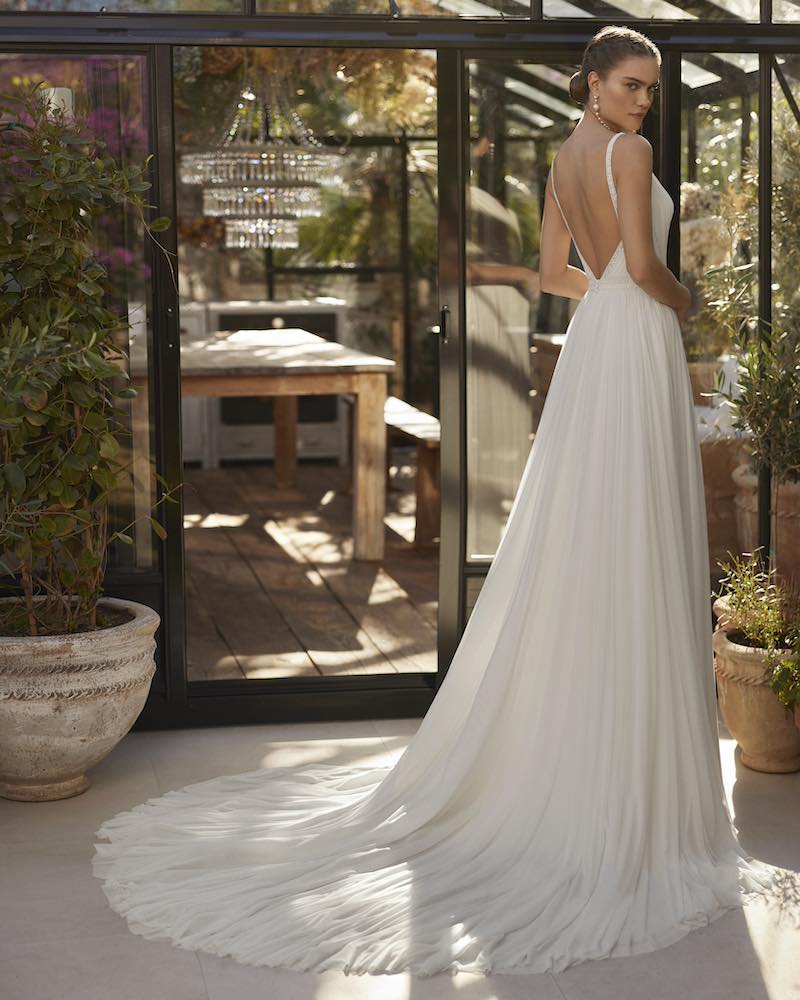 In questa foto una modella posa di spalle indossando un abito da sposa Aire Boho 2025 con scollatura sulla schiena e gonna in cady