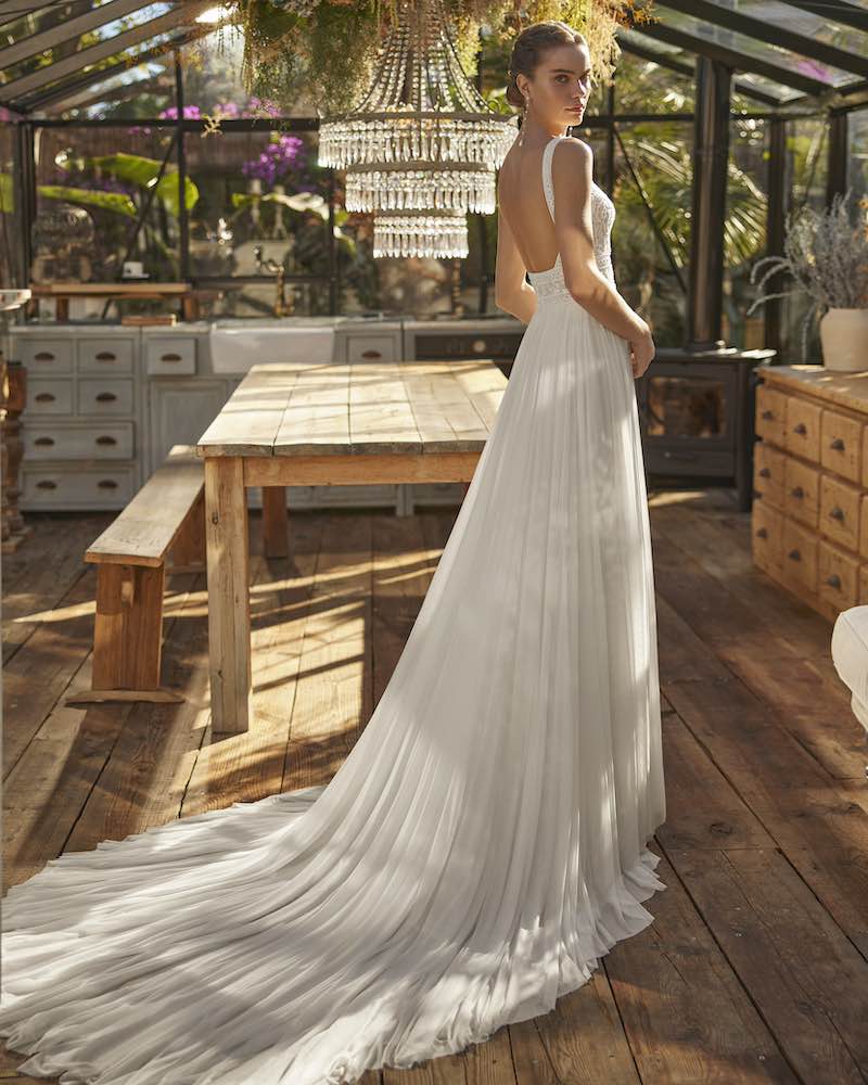 In questa foto una modella posa di spalle indossando un abito da sposa Aire Boho 2025 con scollatura sulla schiena e gonna in cady