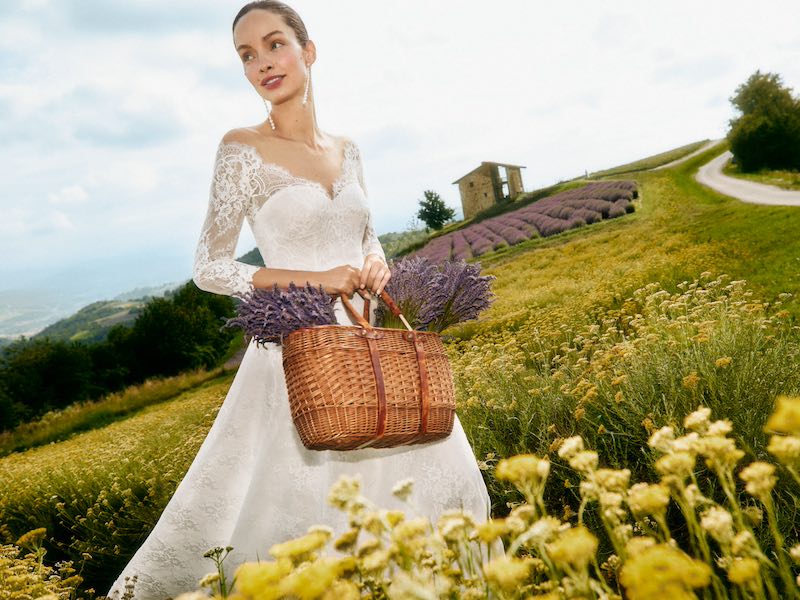 In questa foto, la modella Luma Grothe posa per la nuova campagna Atelier Emé "The Bride" indossando un abito da sposa a A in pizzo tra campi di elicriso e tenendo in mano un cesto di lavanda