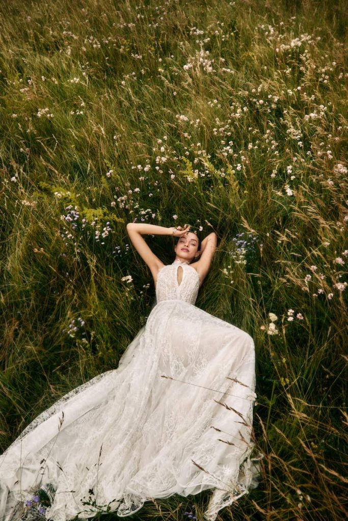 In questa foto la modella Luma Grothe posa sdraiata su un prato indossando un abito della collezione sposa Atelier Emé 2025