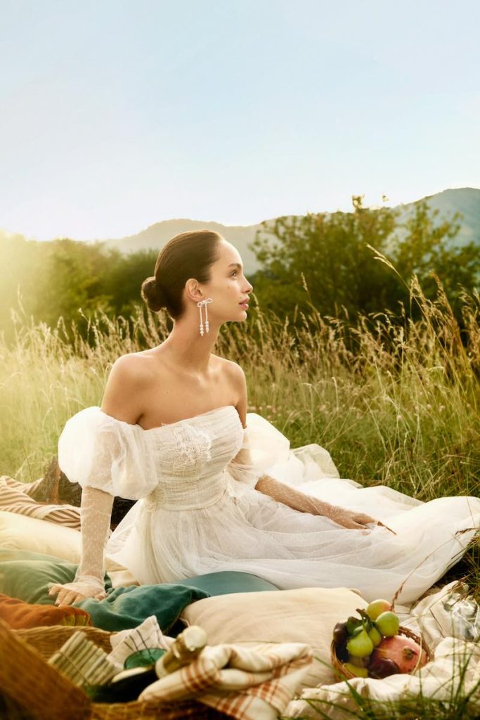 In questa foto la modella Luma Grothe posa per la nuova campagna di Atelier Emé "The Bride" indossando un abito da sposa con maniche balloon, seduta su un prato per un picnic