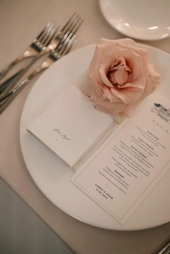 In questa foto un dettaglio della mise en place del matrimonio di Carrie e Adam per cui Imène Hanafi ha usato una rosa come segnaposto e un menù  dalla grafica semplice e lineare