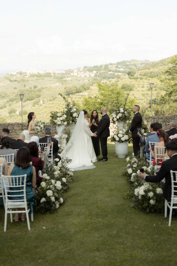 In questa foto una celebrante legge un discorso durante la cerimonia di due sposi in un giardino