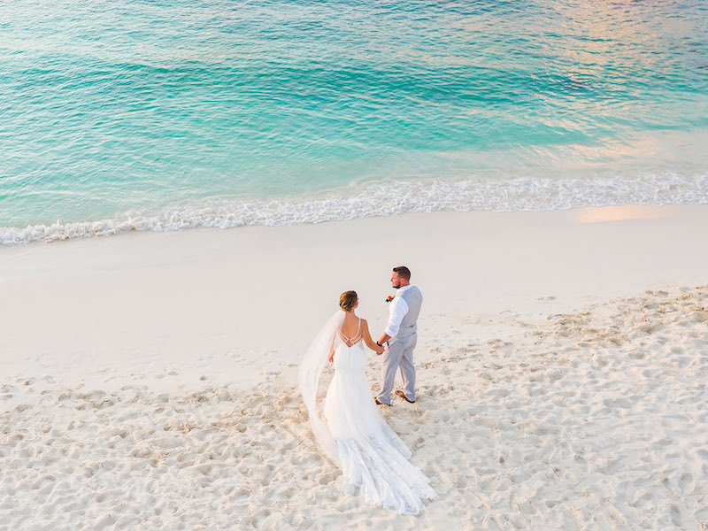 In questa foto, due sposi passeggiano verso il mare su una spiaggia bianca di Aruba