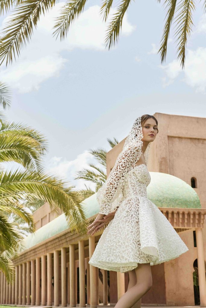 In questa immagine un modello di abiti da sposa corti 2025, interamente ricamato in pizzo, che fa parte della collezione di Elisabetta Polignano.