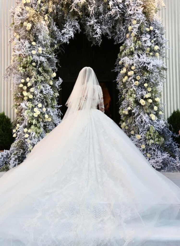 In questa foto, una sposa di spalle entra attraverso l'ingresso di una chiesa decorato con fiori bianchi dalal wedding planner Cira Lombardo