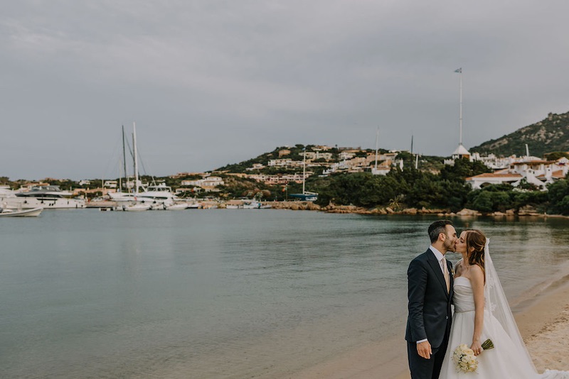 In questa foto due sposi si baciano  sullo sfondo del mare della Sardegna