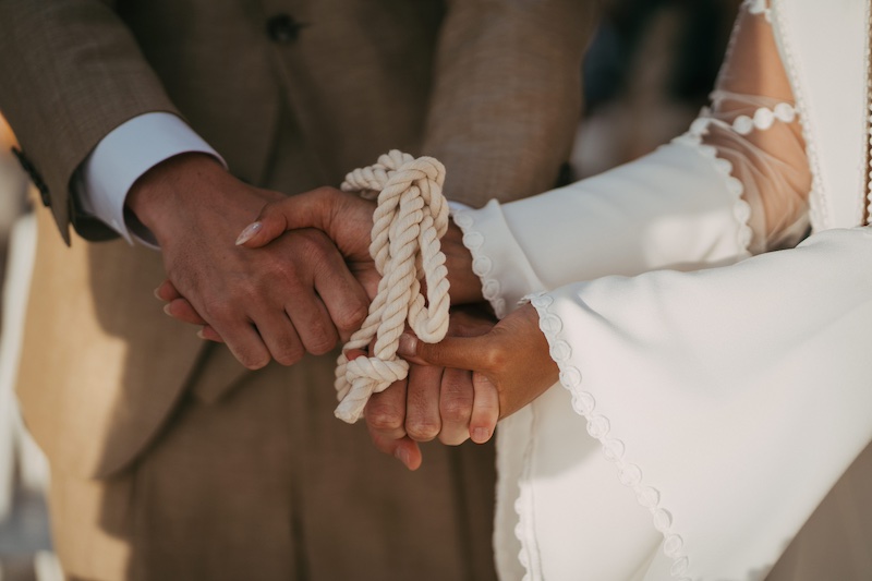 In questa foto il dettaglio delle mani di due sposi che si stringono durante un rito simbolico con una corda