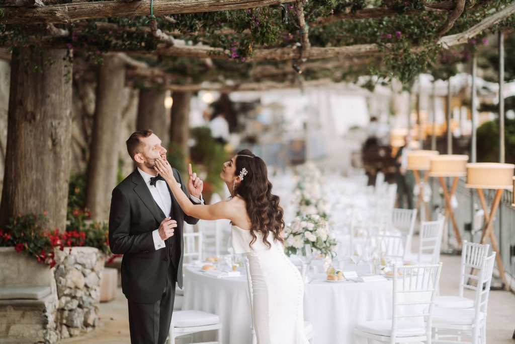 In questa foto una coppia di sposi con i tavoli del matrimonio del wedding planner L'aura Bianca 