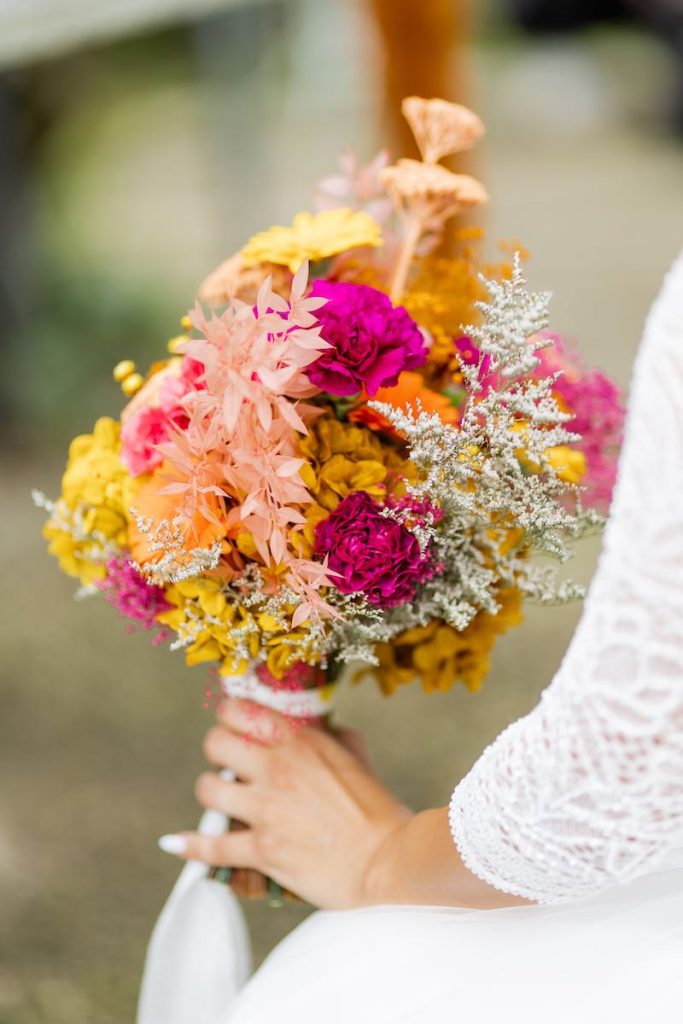 In questa foto, un bouquet da sposa nei toni del fucsia, del giallo e del rosa pesca