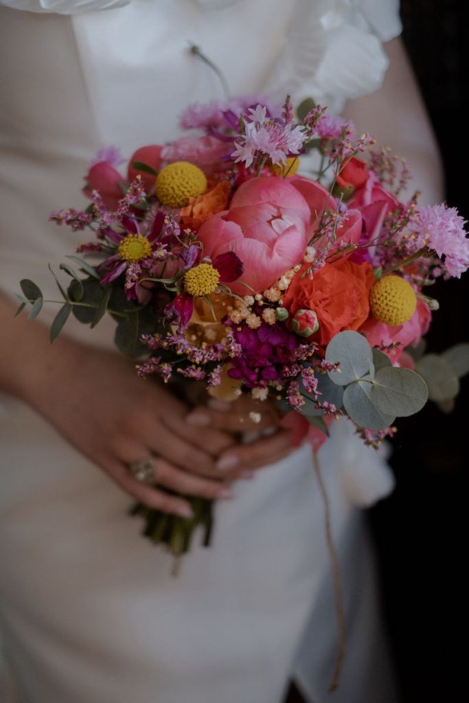 In questa foto, un bouquet da sposa 2025 nei toni del fucsia, arancione e giallo