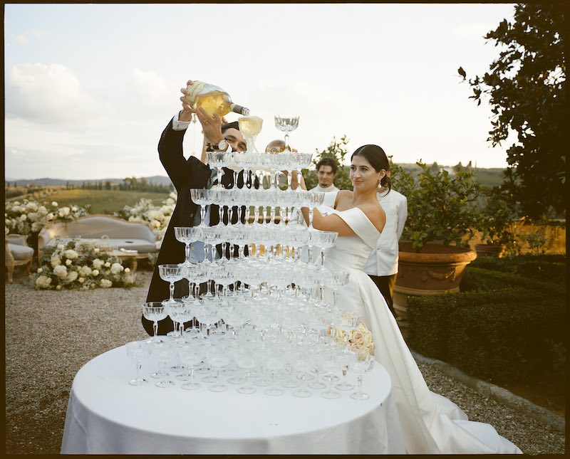 In questa foto, due sposi riempiono le coppie di una Champagne Tower allestita a Villa Corsini