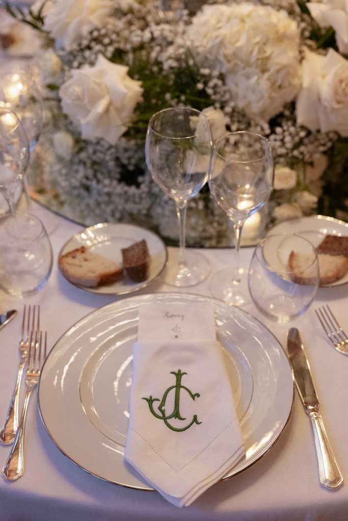 In questa foto, una mise en place per matrimonio allestita dal team di Corsini.Events con tovagliolo di colore bianco personalizzato con le iniziali degli sposi e un centrotavola di fiori di colore bianco