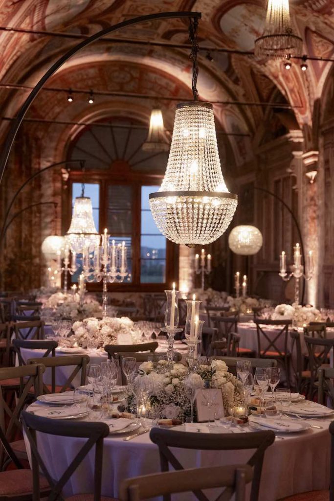 In questa foto, un dettaglio della Galleria di Villa Corsini a Mezzomonte allestita per un matrimonio con lampadari, tavoli rotondi, fiori bianchi e tovagliato en pendant